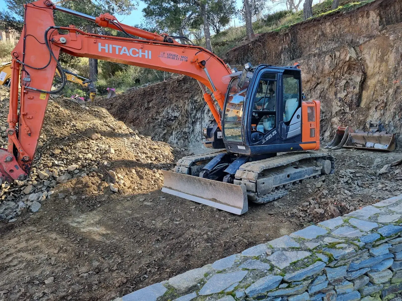 Pelle Hitachi le long du mur en pierre - Banyuls-sur-Mer